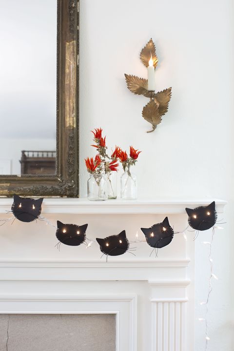 diy halloween garland with paper black cat faces strung on string lights used as indoor mantel decoration