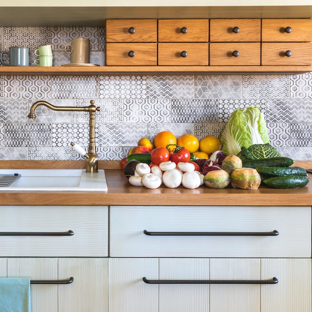 stack of edible mushrooms, vegetables and fruits tomatos, avocado, zucchini, oranges, apples, grapefruits, kohlrabi, chinese cabbage, savoy cabbage, cucumbers, radicchio on countertop in modern rustic kitchen