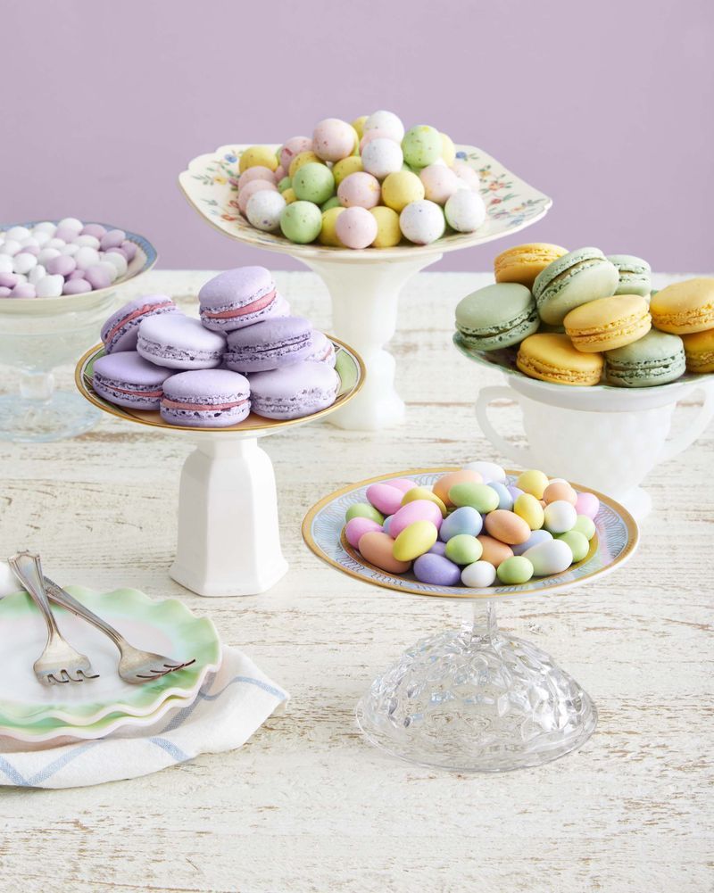 Pastel colored candies and macarons are placed on a candy stand made from vintage plates attached to a pedestal