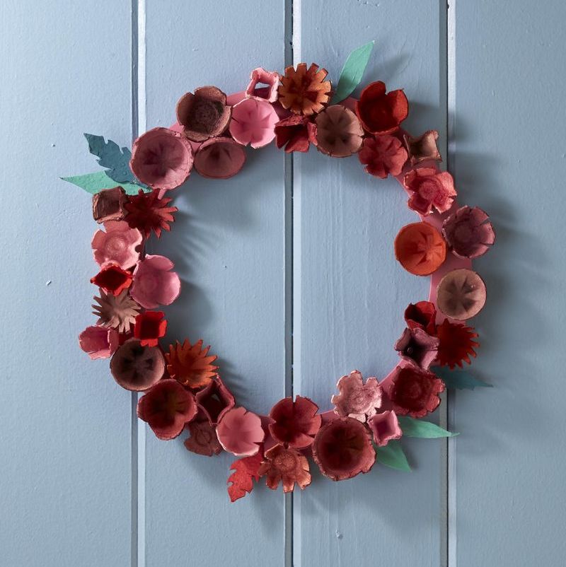 This DIY wreath is made by cutting paper egg cartons into flower shapes, painting them in red and pink hues, and accenting them with green paper leaves.