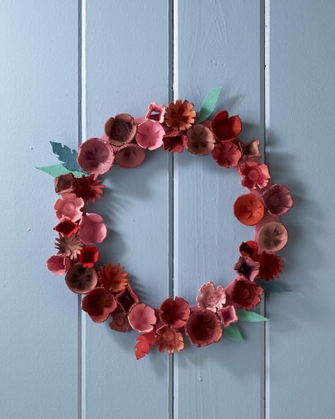 diy wreath made from cups of a paper egg carton cut into flower shapes and painted shades of red and pink and accented with green paper leaves
