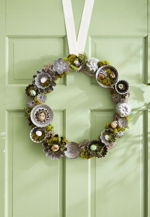 moss wreath decorated with small baking tins and quail eggs, pictured on a pale green door