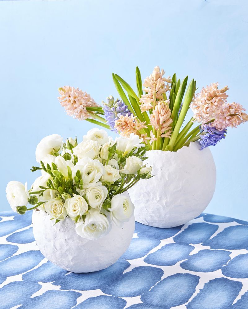A white papier-mache egg-shaped vase filled with flowers was decorated with an abstract blue and white tablecloth