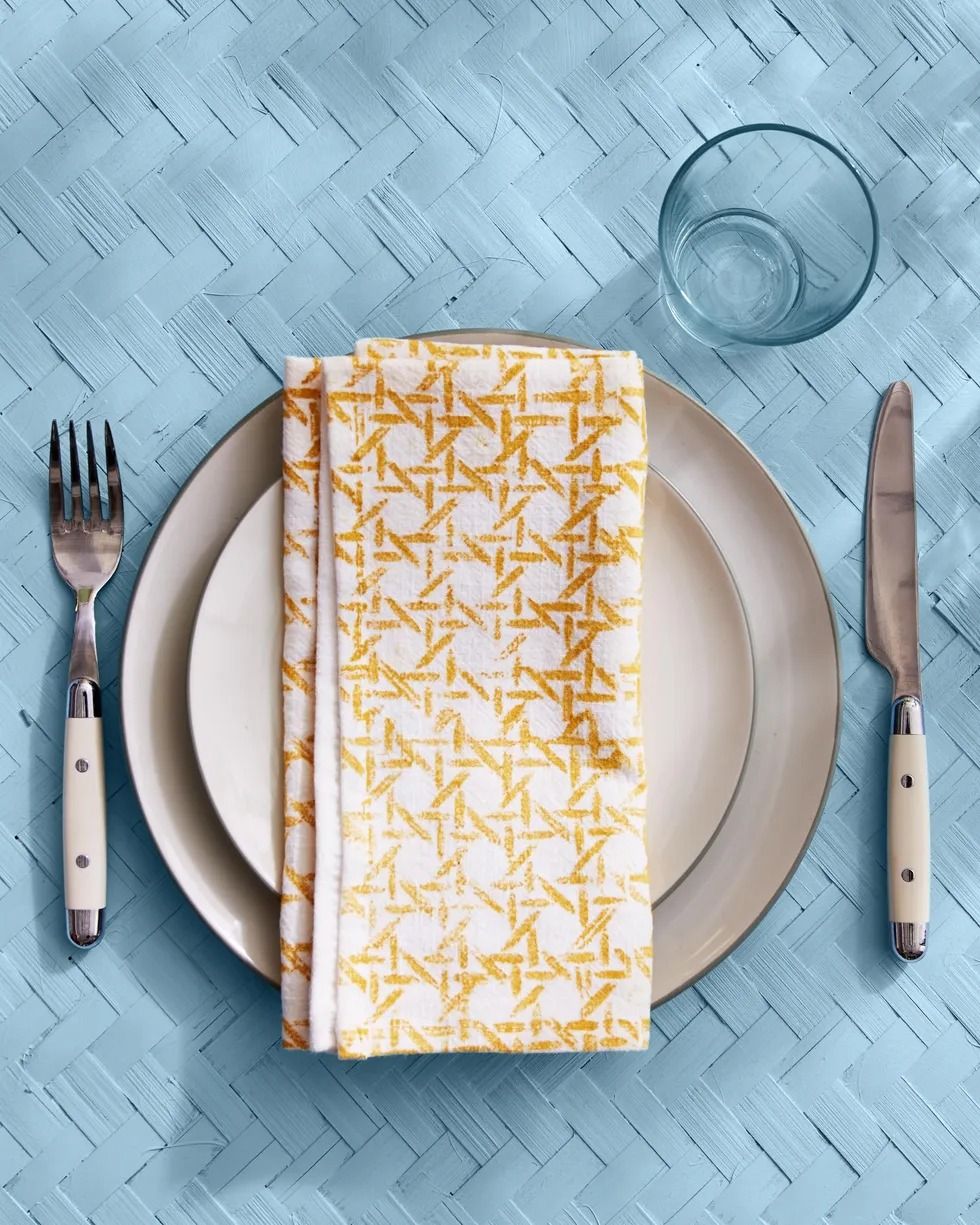White napkin engraved with a folded yellow cane pattern on a simple stand on a pale blue textile surface