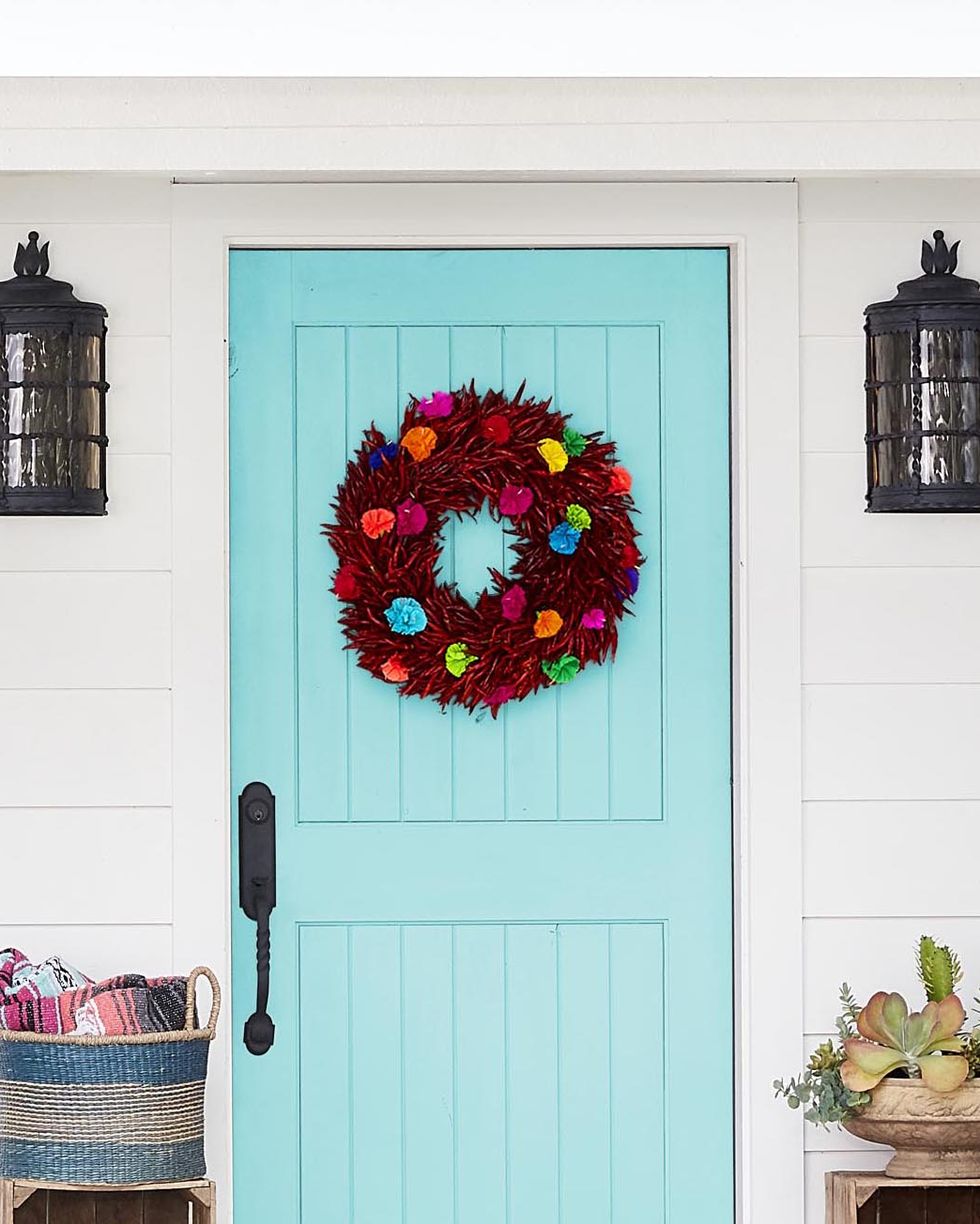 a wreath made from chili peppers and tissue paper flowers hung on a light blue door