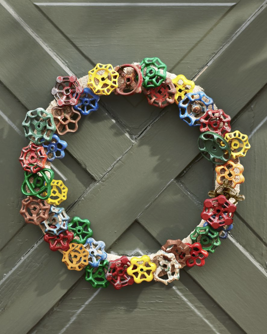 colorful vintage garden faucet handles attached to a wreath form hung on a green door