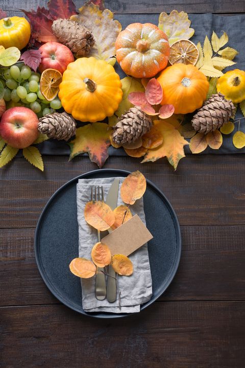 fall table place setting with orange dry leaves and pumpkins vertical format centerpieces thanksgiving day view from above