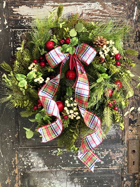 a greenery wreath with red  and white berries plus a large tartan bow