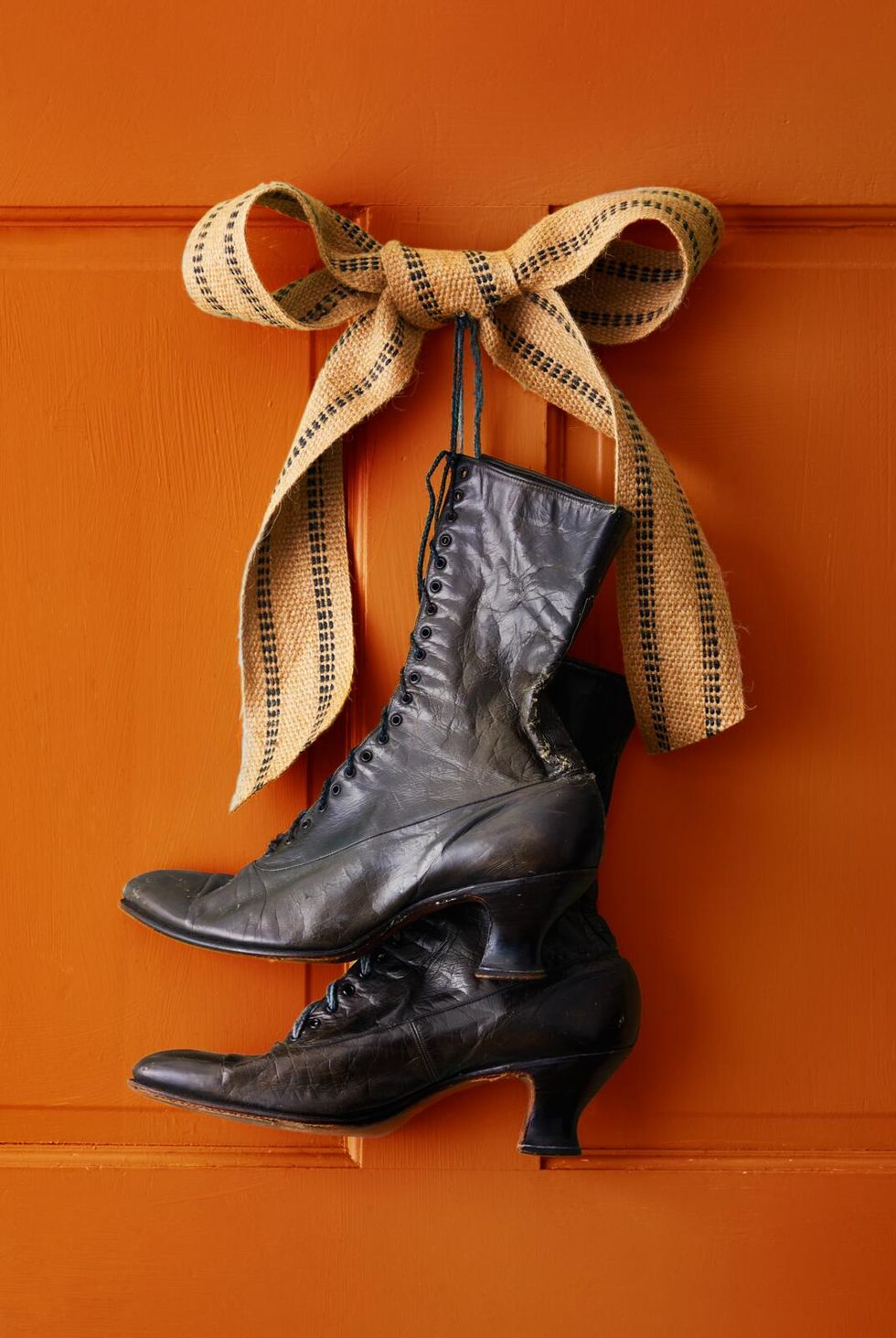 victorian style black boots hung on an orange door with a burlap bow in celebration of halloween