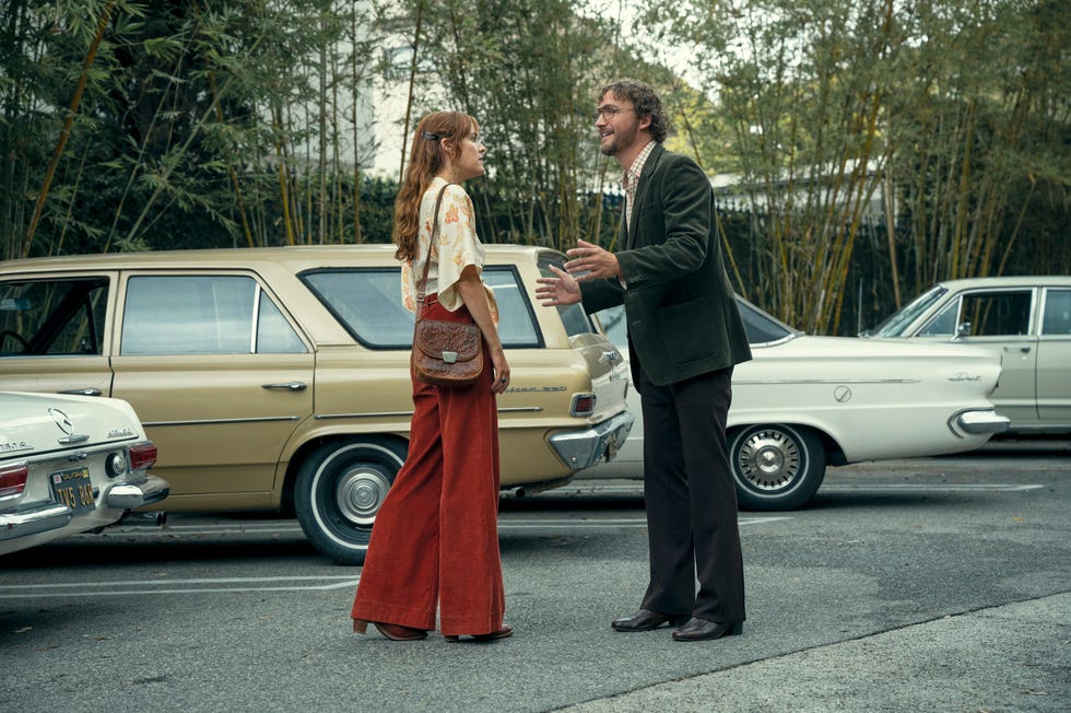 riley keough dressed in orange pants and floral blouse in daisy jones and the six