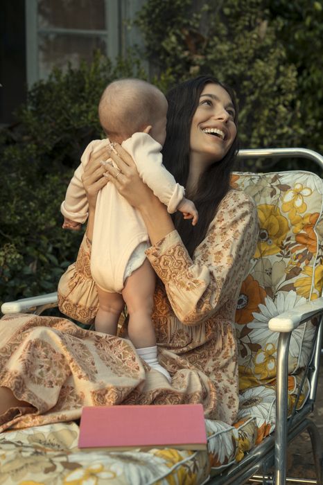 camila morrone camila wearing a dress and holding a baby in a guide to the daisy jones and the six costumes