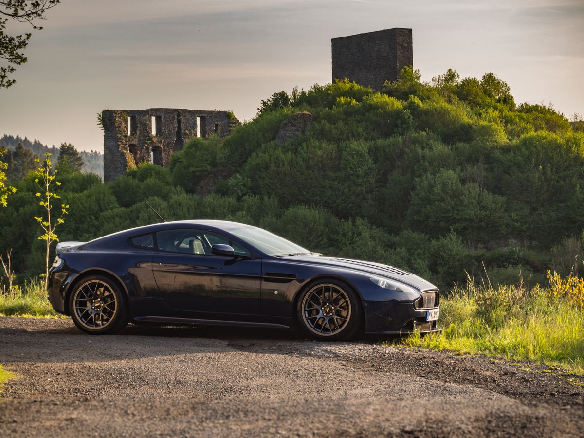 a 2007 aston martin v8 vantage in front of a green hill in germany