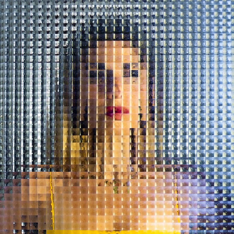 woman in a yellow vest behind distorted glass giving the impression she's been pixelated or censored