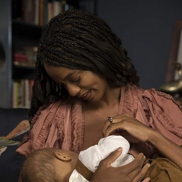 a woman nursing a baby on a dockatot nursing pillow