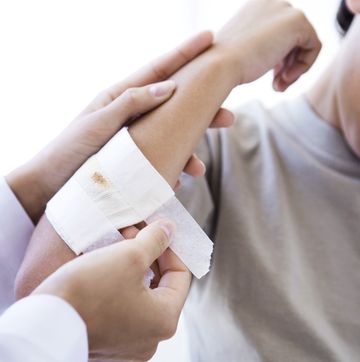 Doctor applying gauze to child's arm, cropped view