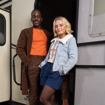 doctor who stars ncuti gatwa and millie gibson in costume on set, posing on the steps of a trailer for a first look photo