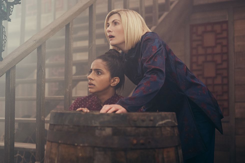 mandip gill as yaz and jodie whittaker as the doctor in doctor who, two women crouching behind a barrel looking worried and frightened