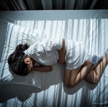 woman holds her stomach as she curls up in bed looking pained