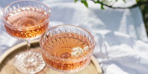 two glasses of rose wine outdoors on wooden tray and white textile, picnic in spring sunny day, green grass and blossoming cherry trees