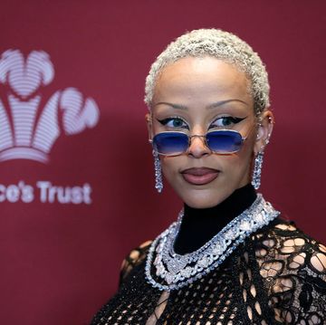 doja cat looks to the right, she wears a black lace top with diamond and silver jewelry and blue tinted glasses