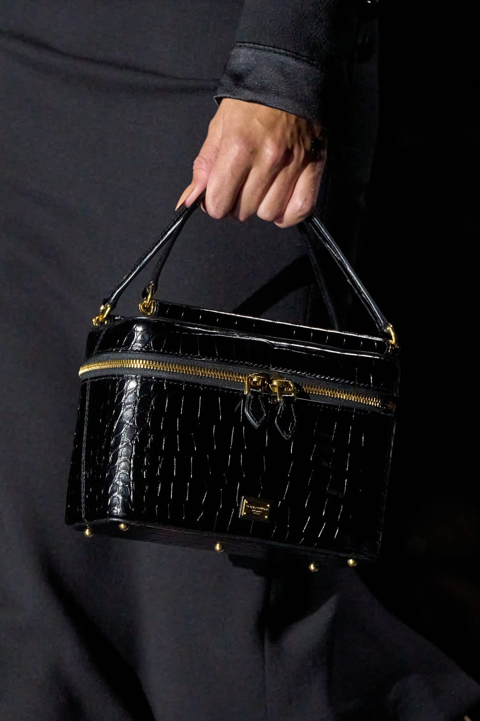 Stylish black crocodilepatterned handbag held by a hand