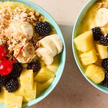 pineapple dole whip smoothie bowl in a blue bowl topped with pineapple, banana, blackberries, cherries, and toasted coconut flakes