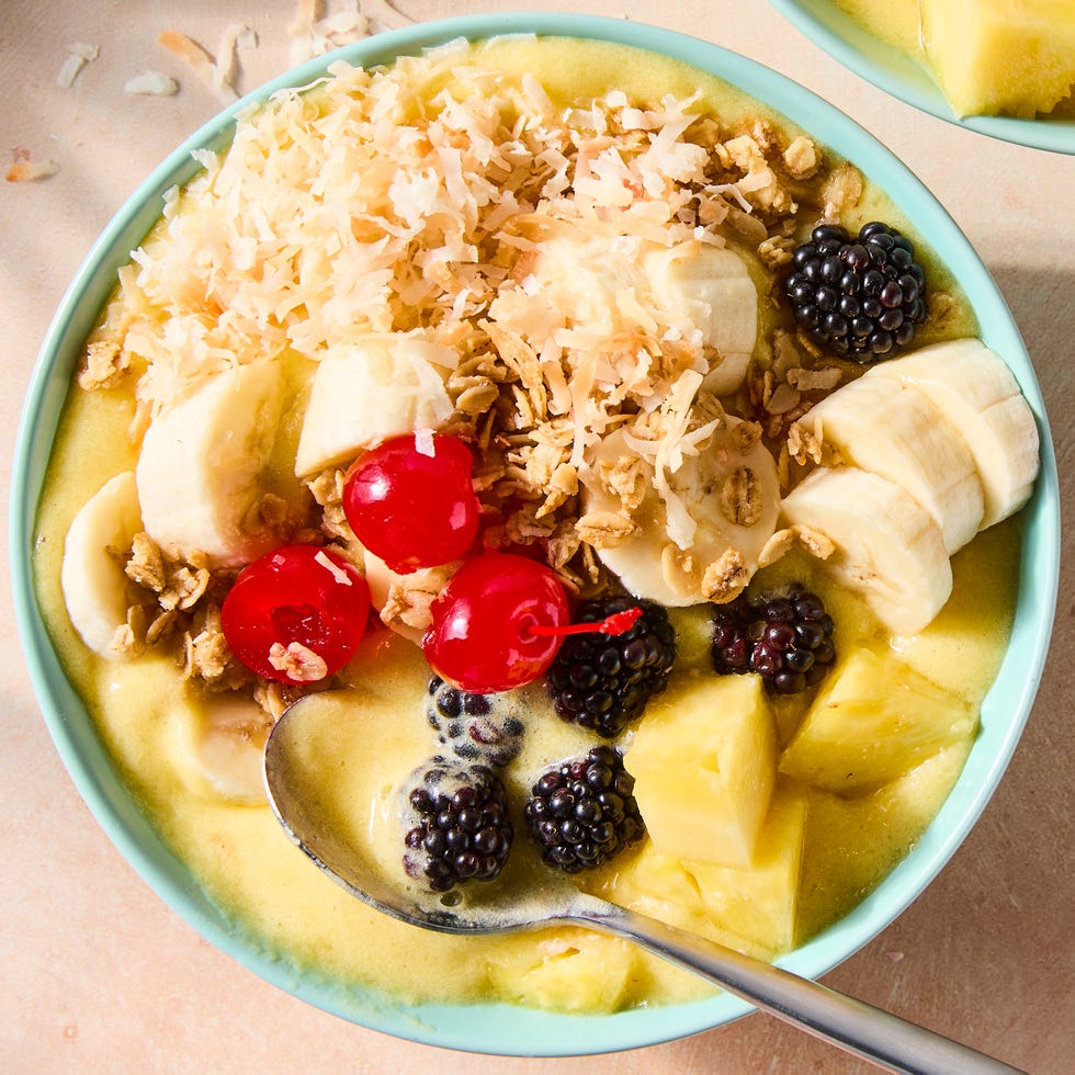 pineapple dole whip smoothie bowl in a blue bowl topped with pineapple, banana, blackberries, cherries, and toasted coconut flakes