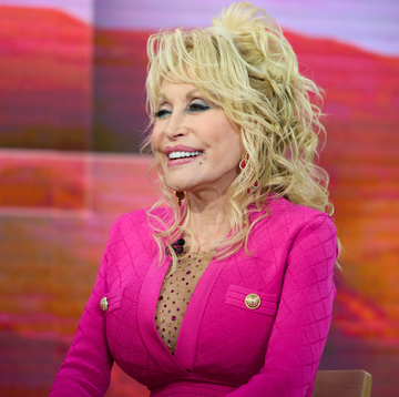 dolly parton wearing a pink shirt smiling, next to a pink bottle of perfume