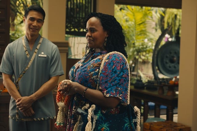 two individuals in a tropical setting one wearing a colorful patterned outfit and the other in a gray uniform