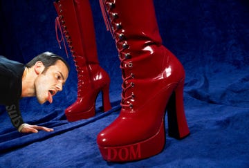 a submissive male licking the red patent leather boots of his dominant partner