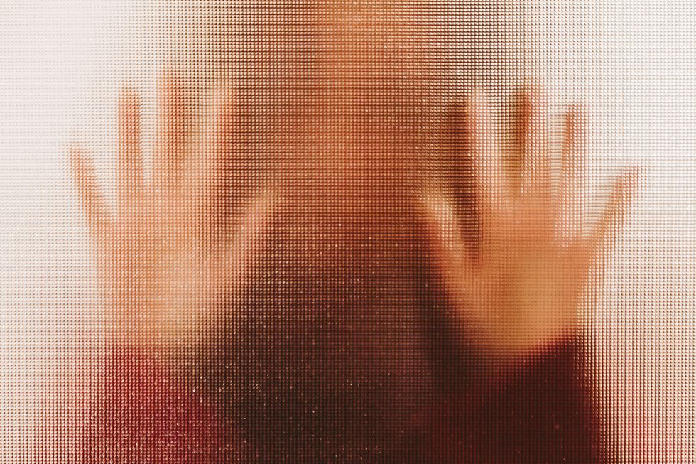 domestic abuse victim with hands pressed against glass window