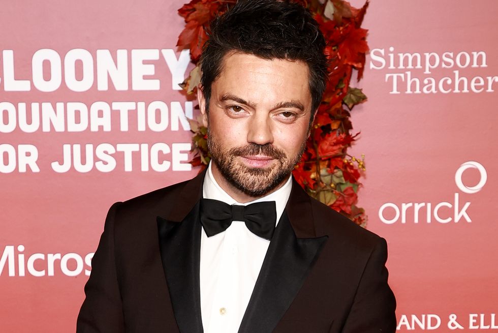 Dominic Cooper wears a black tuxedo and smiles at the camera