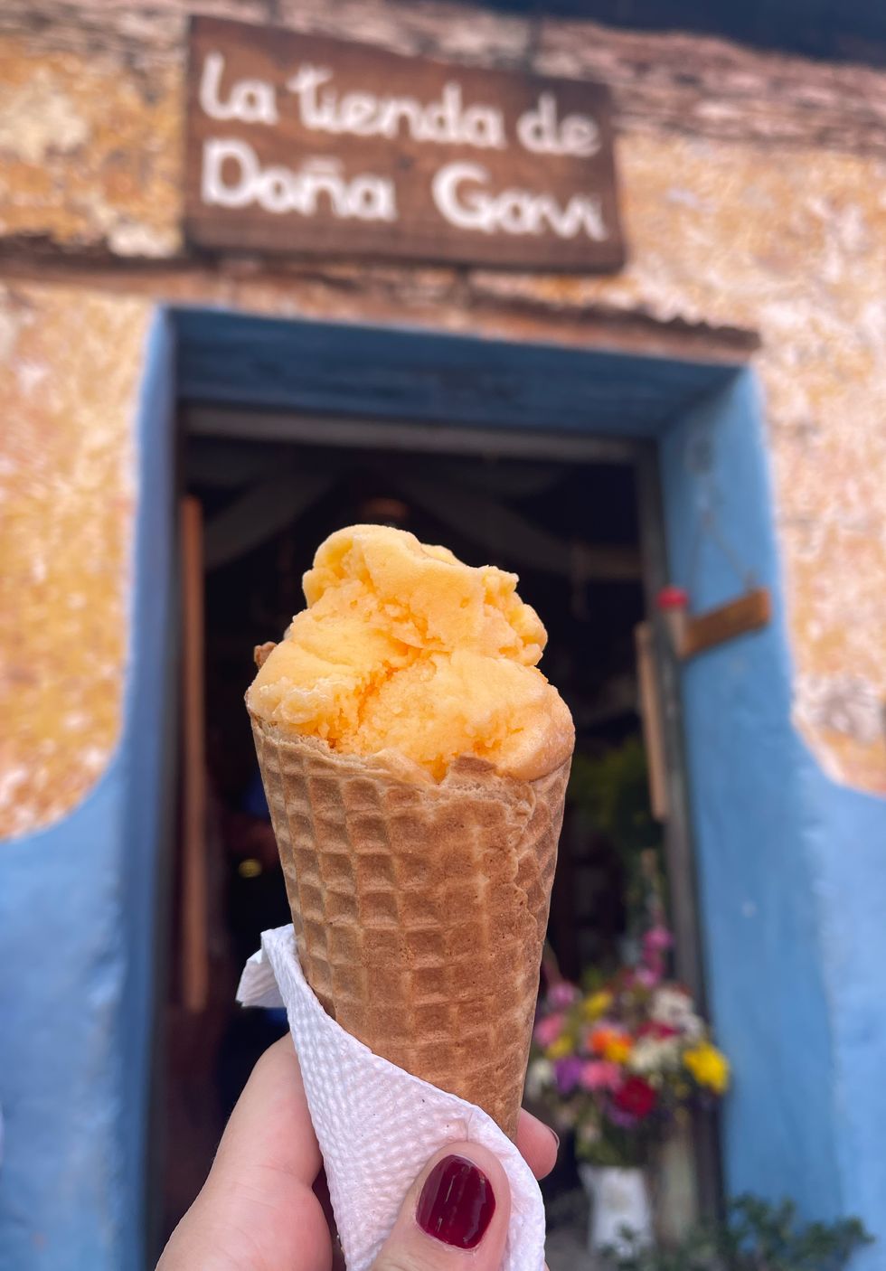 hand holding up an ice cream cone with orange ice cream in front of a sing that says dona gavi
