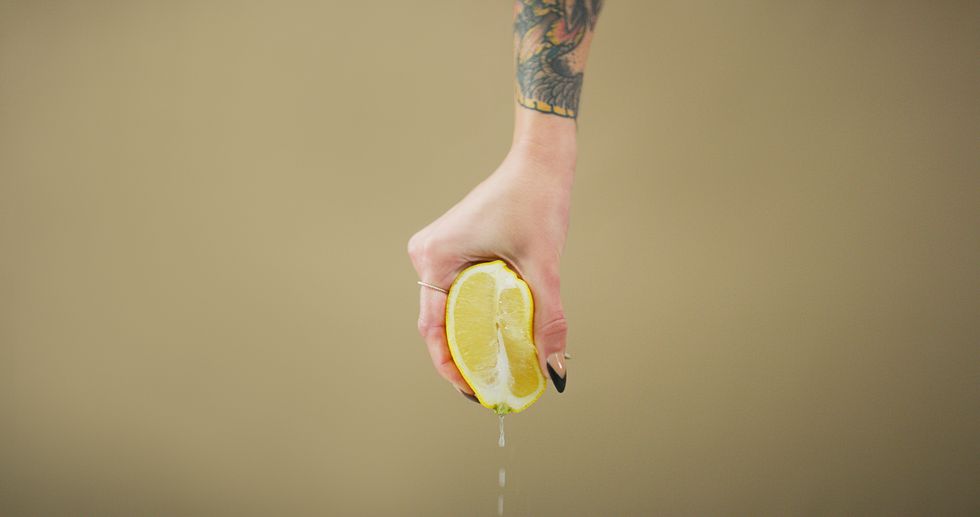 studio shot of a person squeezing a lemon slice against a brown background