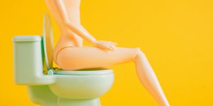 dool sits on green toy toilet bowl on yellow background