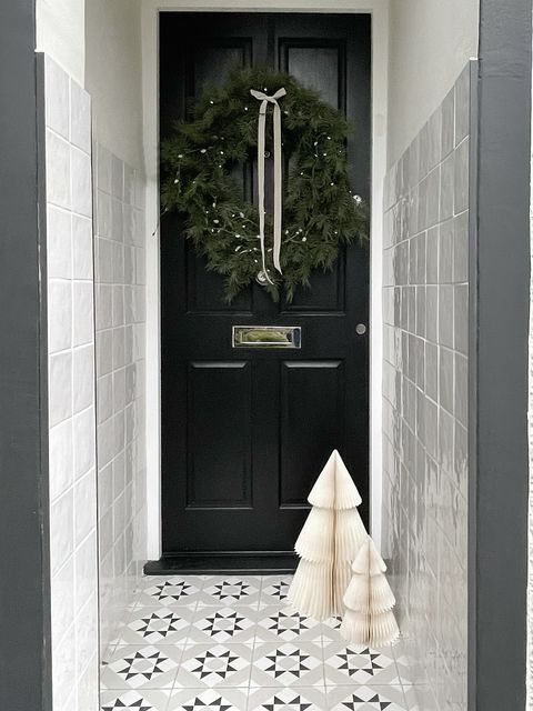 a white hallway leading to a black door with a christmas wreath and small white trees as decor