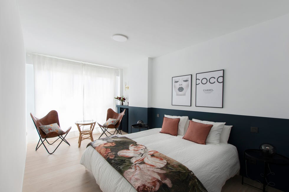 dormitorio con pared a dos colores, textiles florales y dos sillas de piel estilo butterfly