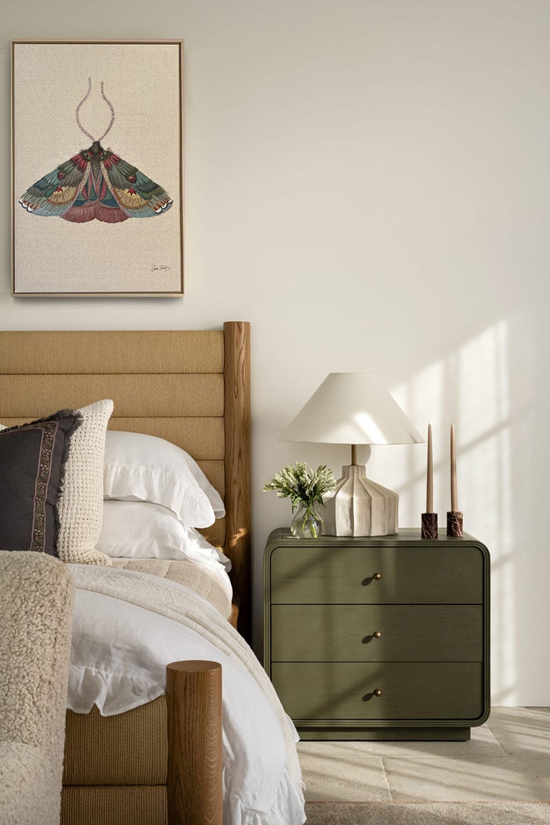dormitorio con cama de pilares de madera y tapizada en color barquillo, ademas de una mesilla verde y cuadro de mariposa en la pared