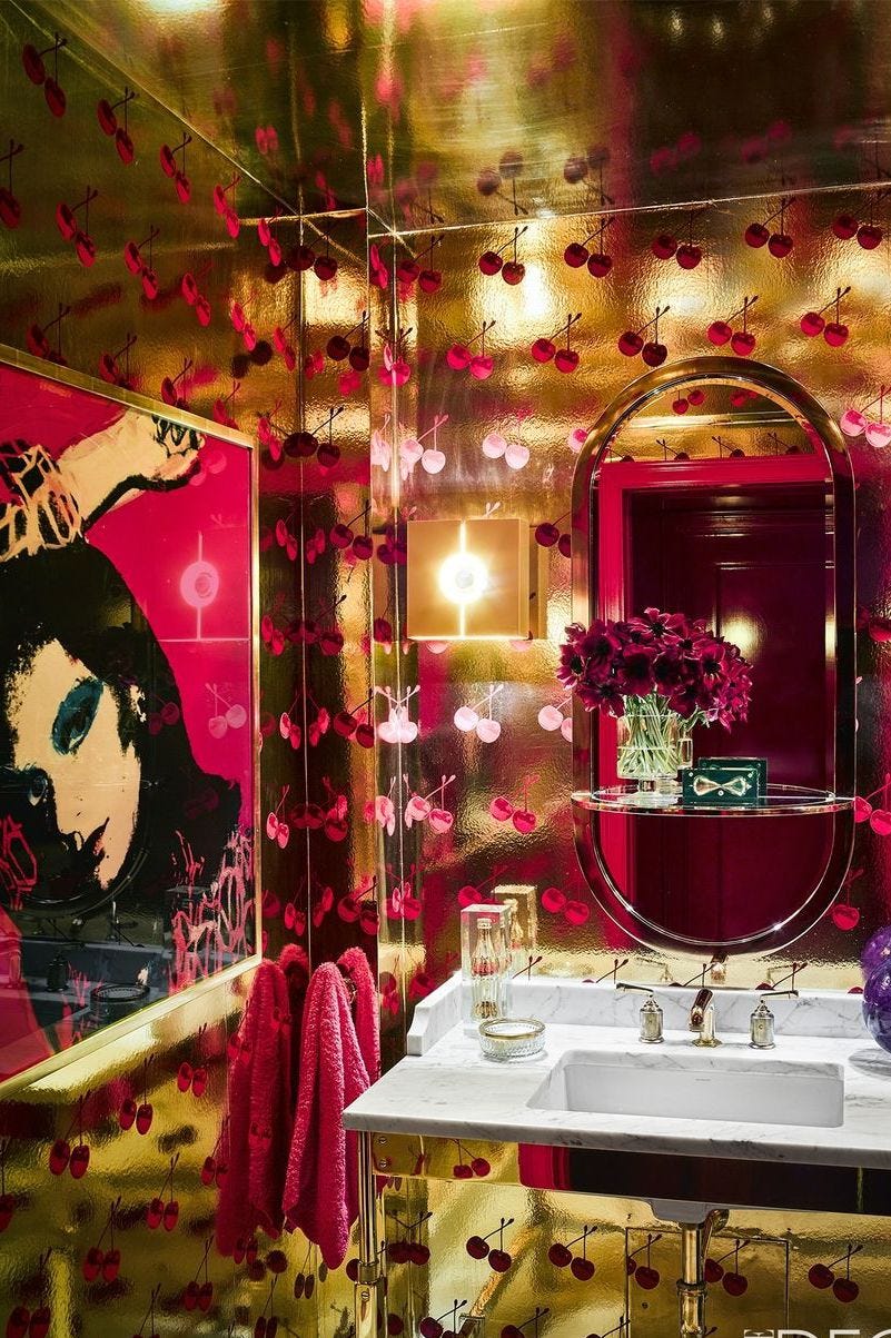 chic bathroom with gold foil wallpaper, a pop art print, an oval shaped mirror, and a shelf with roses on it
