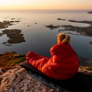 woman in sleeping bag looking over cliff at sunrise