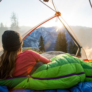 woman in green down sleeping bag looking out of tent at mountains
