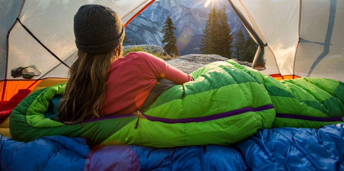 woman in green down sleeping bag looking out of tent at mountains