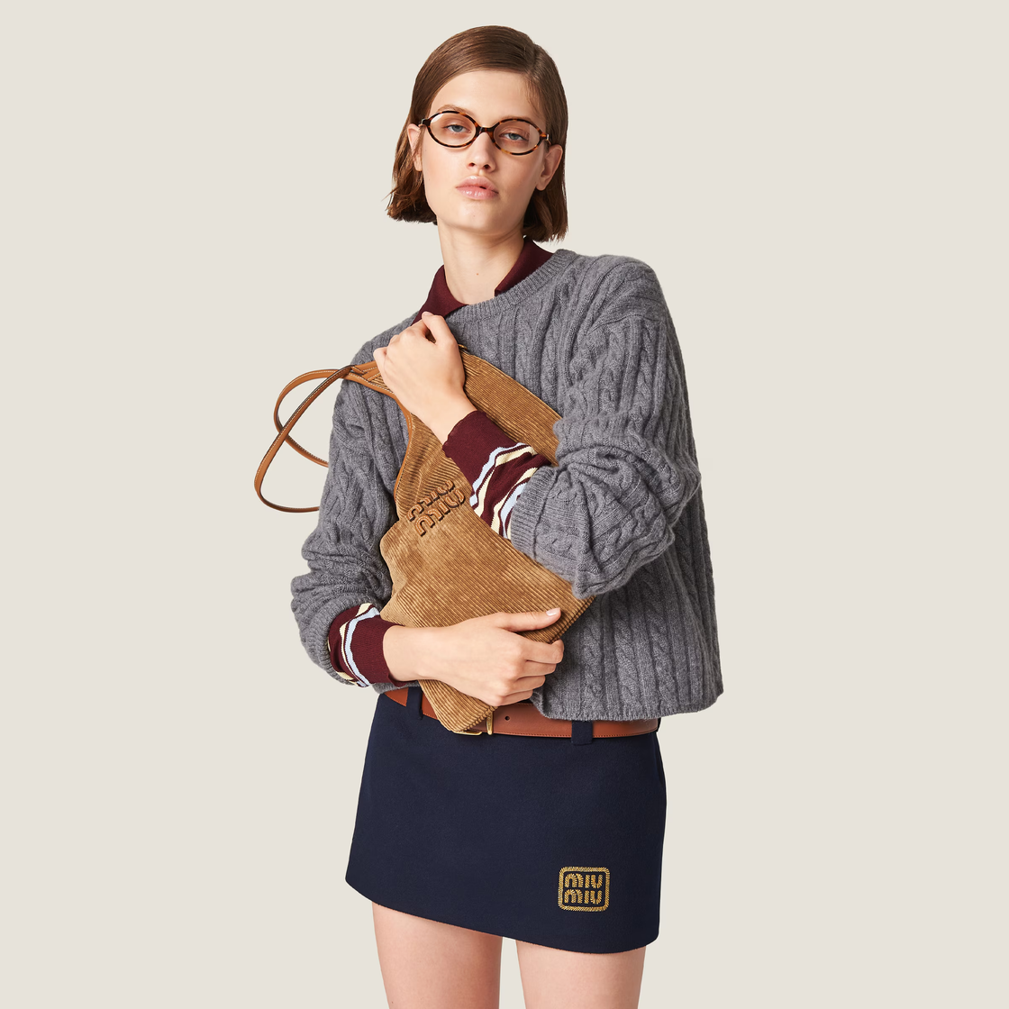 fashion model holding a handbag while wearing a gray cableknit sweater and navy skirt