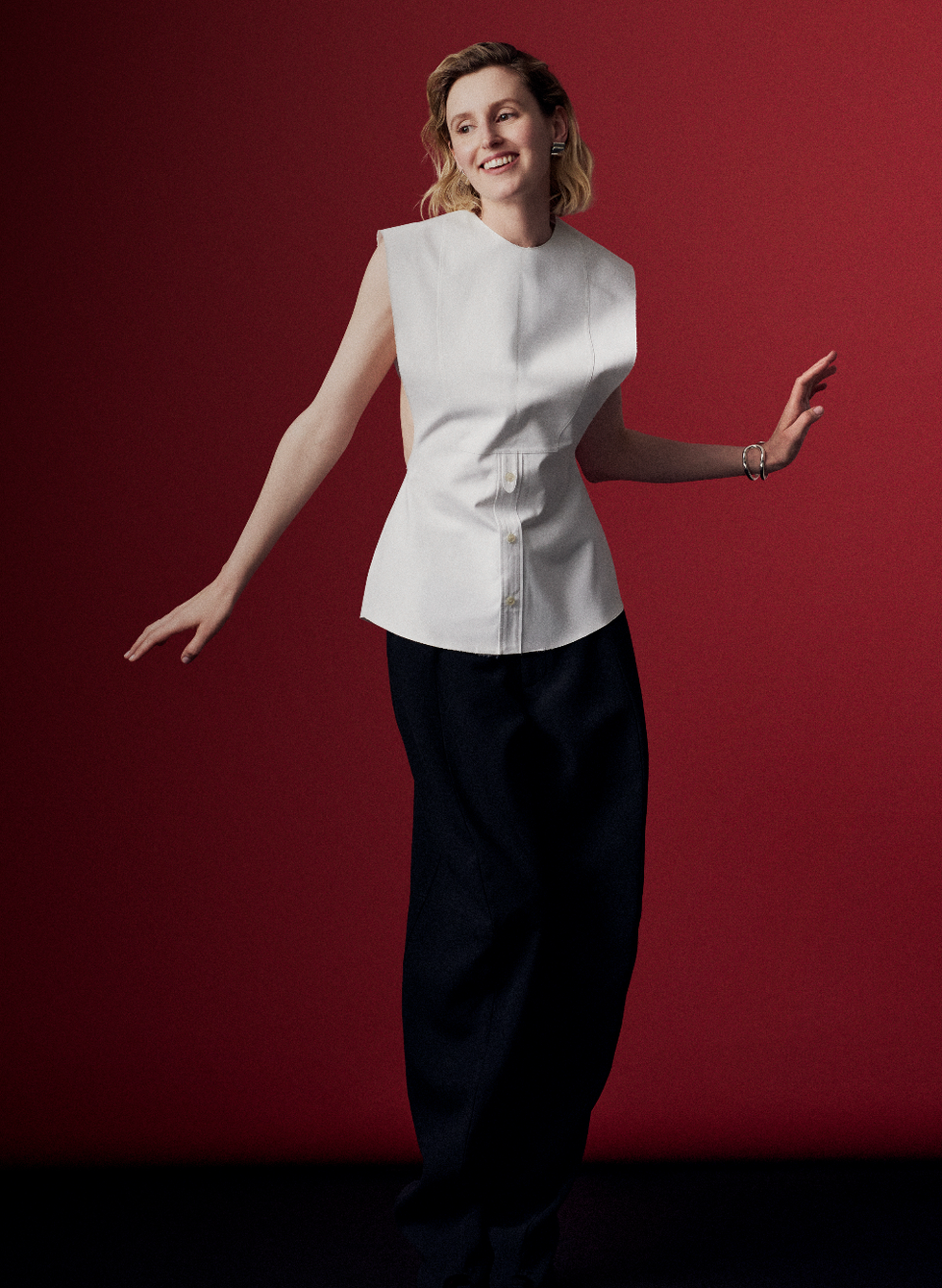 a person wearing a fitted white top and loose black trousers against a dark red background
