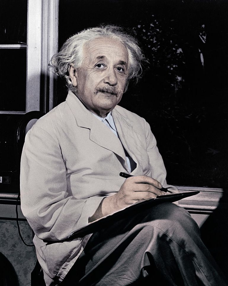 albert einstein sitting by a window and writing on a notepad as he looks up