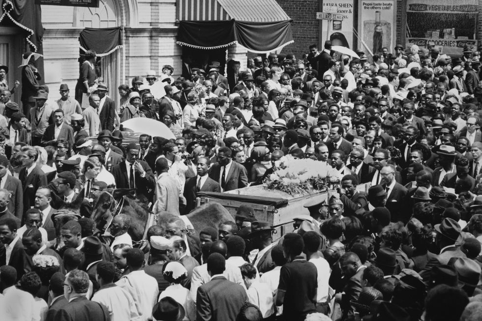 a crowd of people surround a horse drawn cart pulling a casket topped with flowers