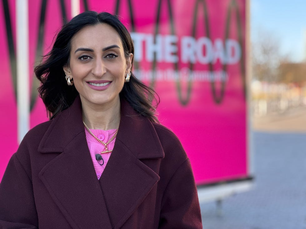 a woman in a maroon coat stands in front of a colorful backdrop