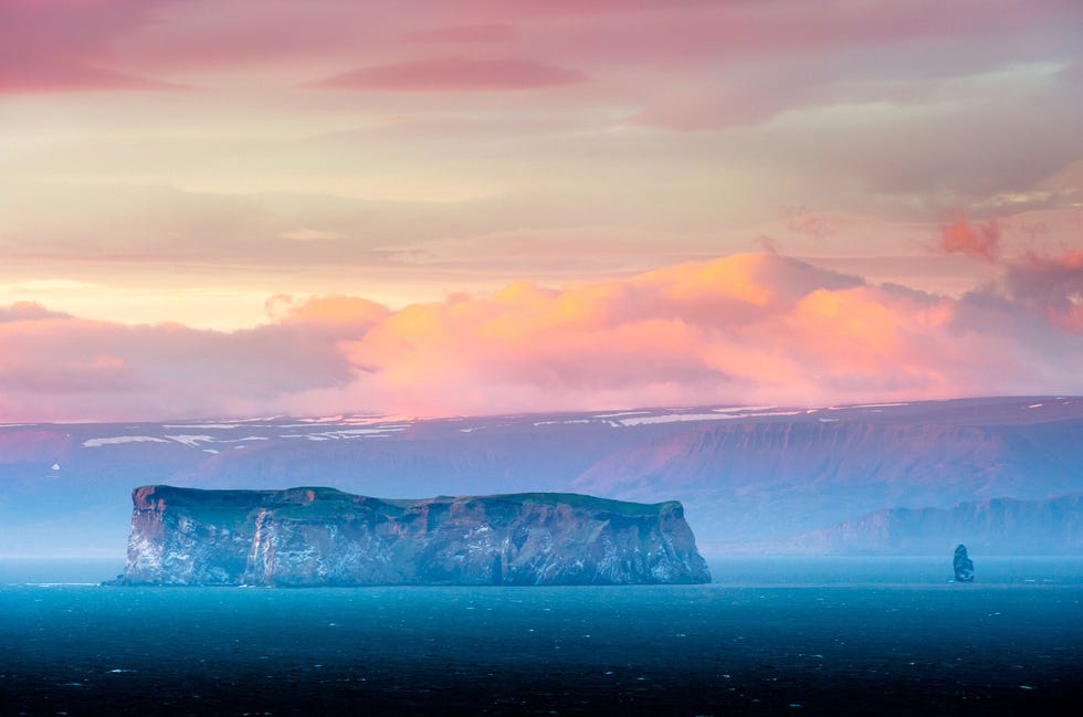 Zalmkleurige en roze wolken hangen boven het eilandje Drangey