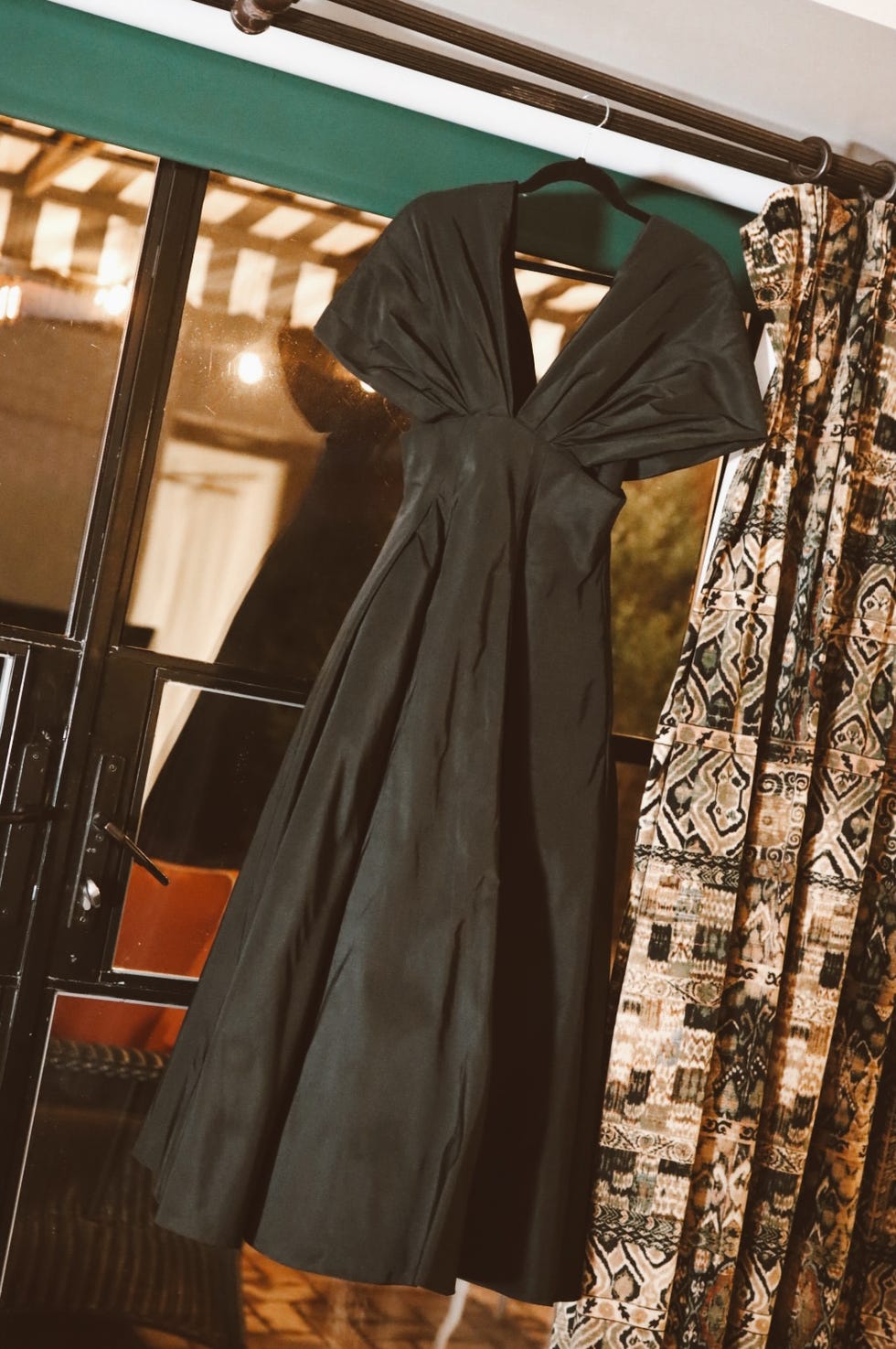 black dress hanging near a patterned curtain