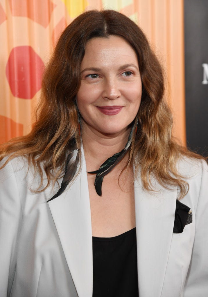 Drew Barrymore wears a white blazer, black top, and long black feather earrings on the red carpet